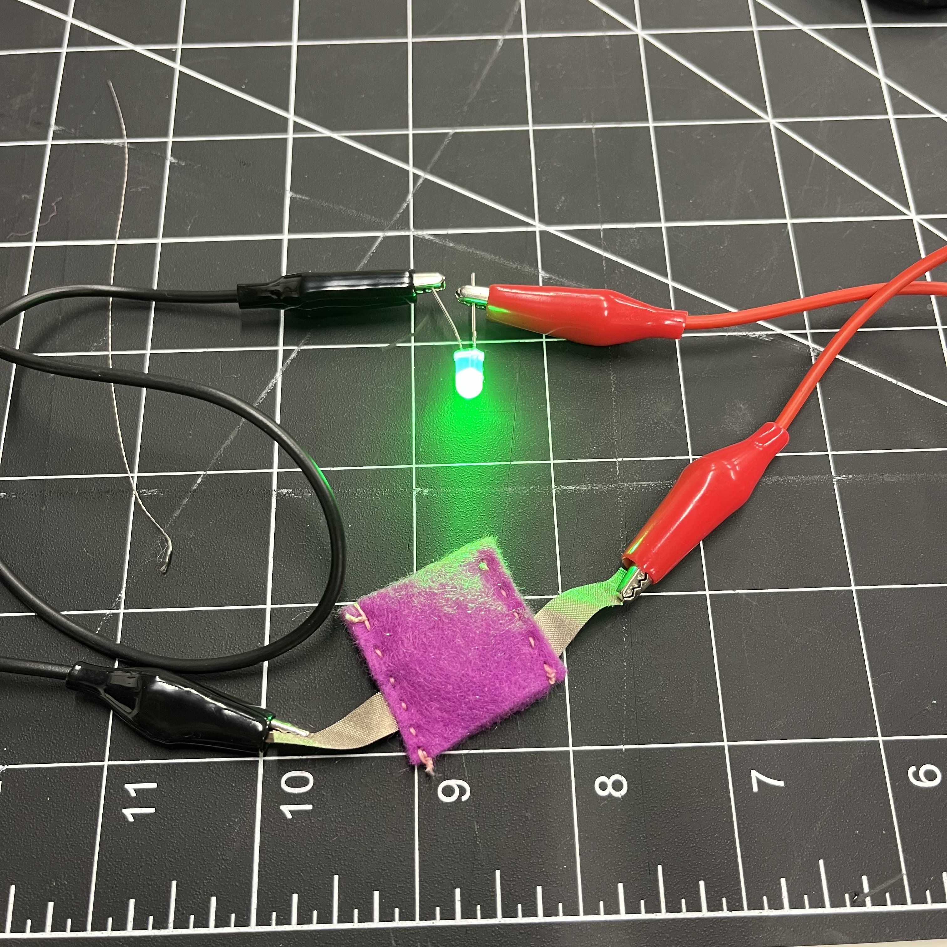 I made a felt battery pouch with conductive fabric cut into ribbons to complete the circuit when a battery it inside of the pouch. I attached alligator clips to the ribbons, and then the clips attach to the correct anode and cathode wires of the LED light.