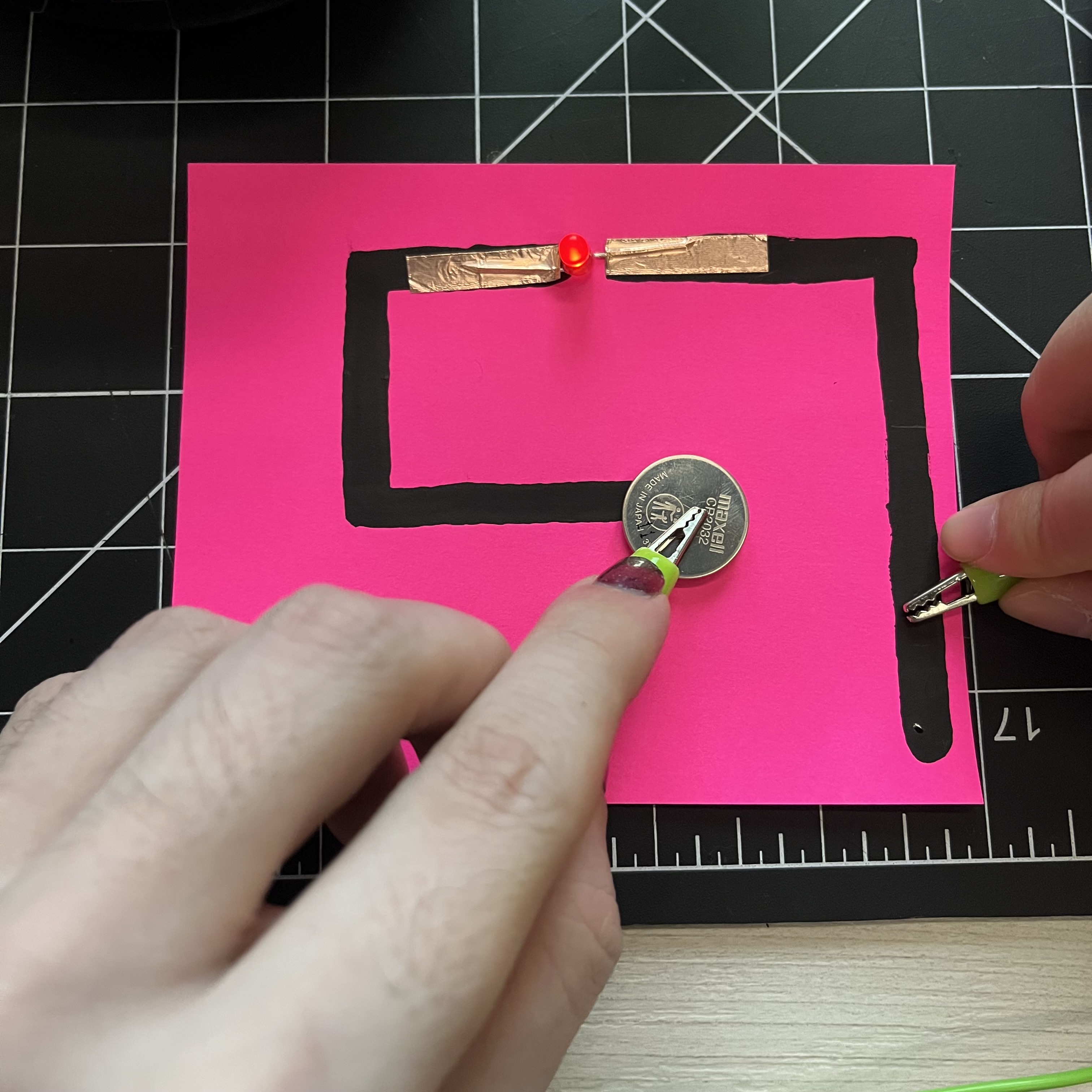 I started exploring with other materials now. This is conductive paint on pink card stock, with copper tape to anchor the light and continue the circuit. Instead of a fold-over to close the circuit, I used the green gator clip with wire and pressed it against the paint. When I had it clamped to the paper it wasn't making enough contact to light up the LEDs so I had to do it this way.